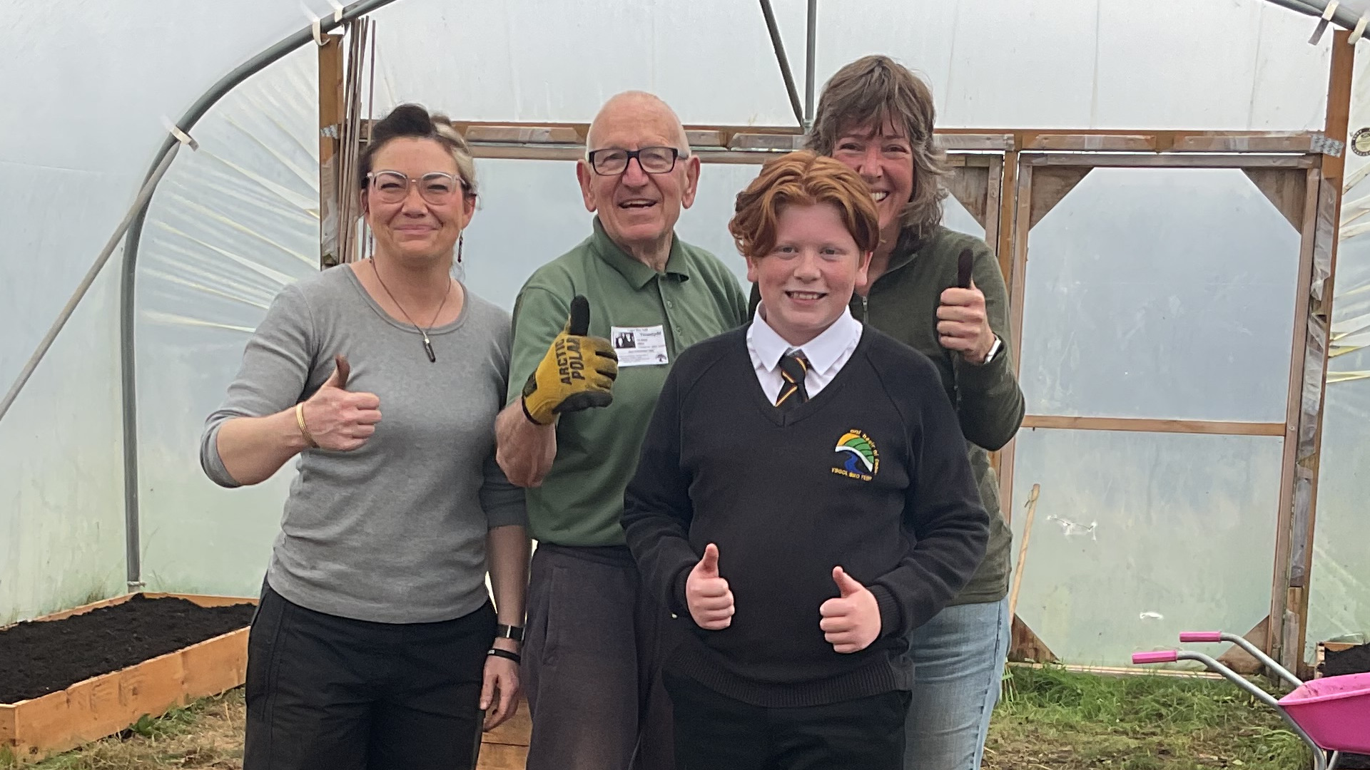 volunteers standing in a polytunnel giving a thumbs up sign